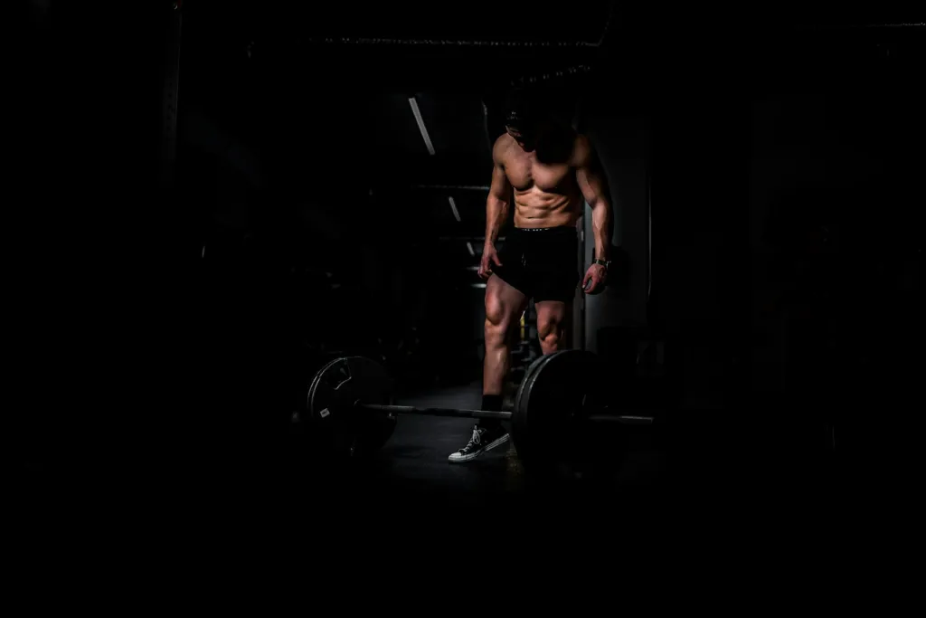 Athlete beside a barbell in a dark gym